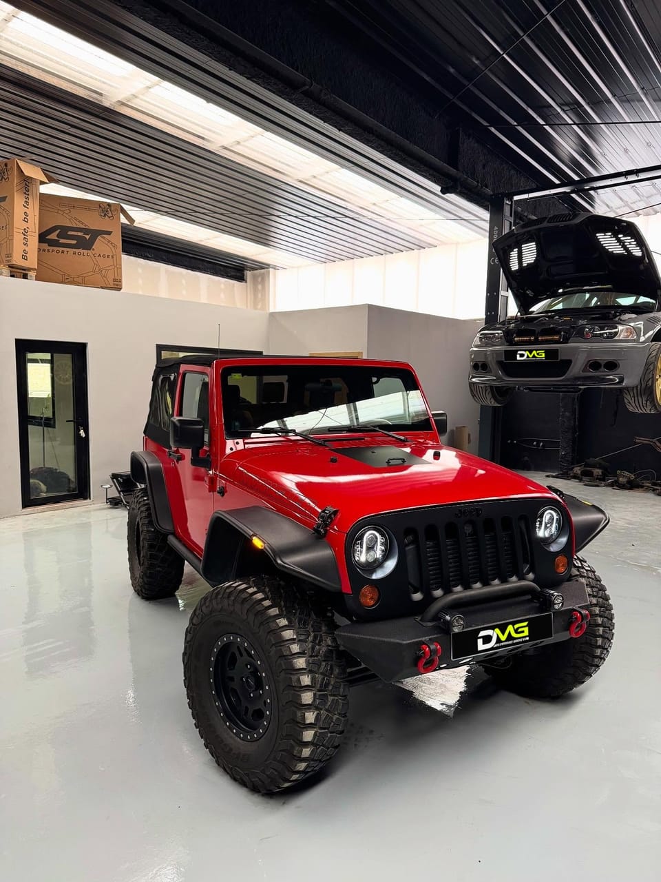 Jeep Wrangler rojo preparado por DMG, con paragolpes de acero y neumáticos de barro, en la nave del taller